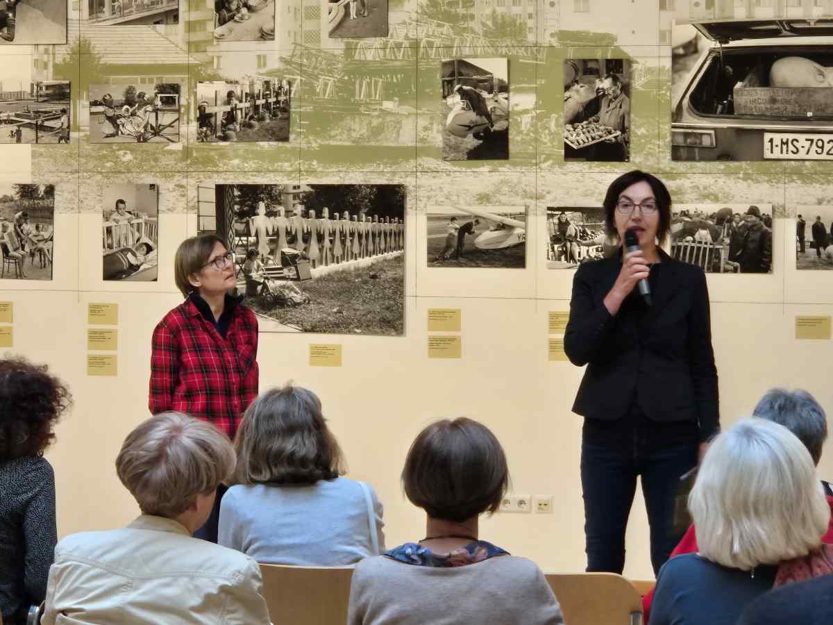 Guy holding a piece of a watermelon with his knife. In the background a girl is watching